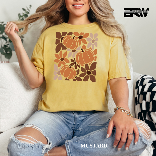 Woman wearing a mustard yellow t-shirt with pumpkin and floral design, sitting on a couch.